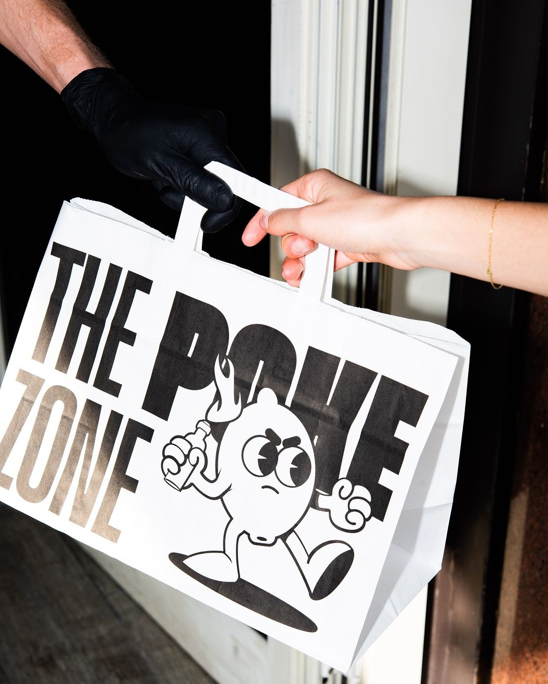 Close-up of a hand receiving a Carrier Bag with Logo from The Poke Zone, featuring a bold graphic design, during a takeaway handoff.