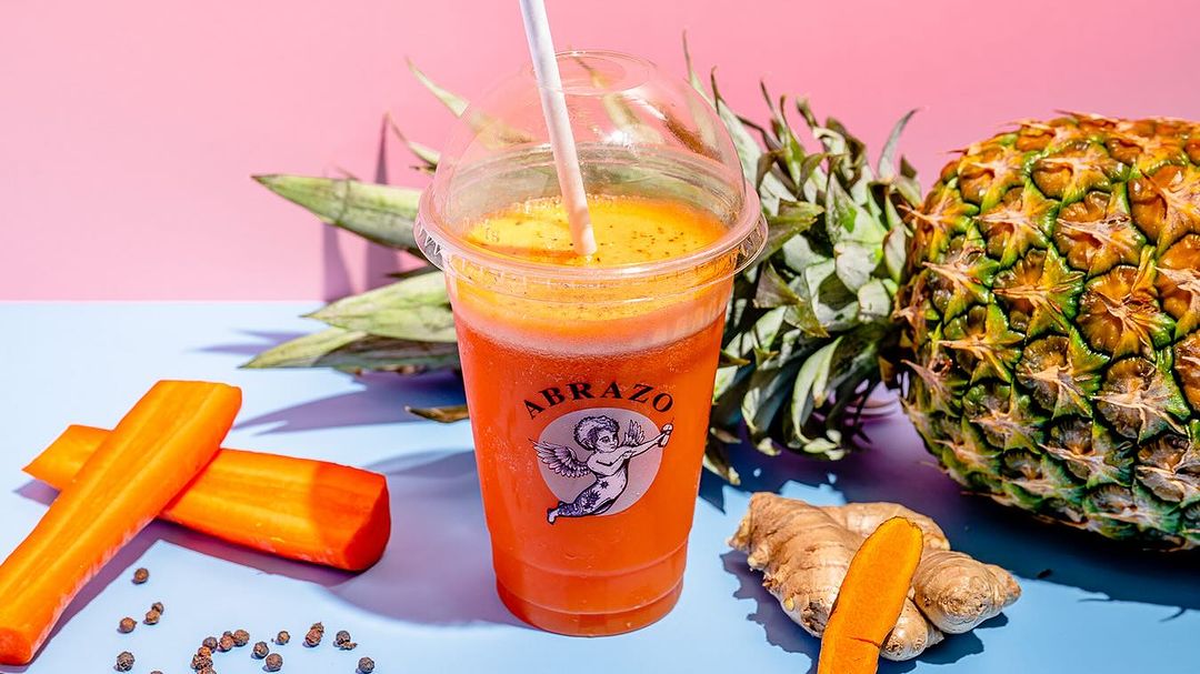 Tropical fruit smoothie in a personalised smoothie cup with Abrazo branding, featuring vibrant ingredients like pineapple, carrot, turmeric, and ginger for a refreshing boost.