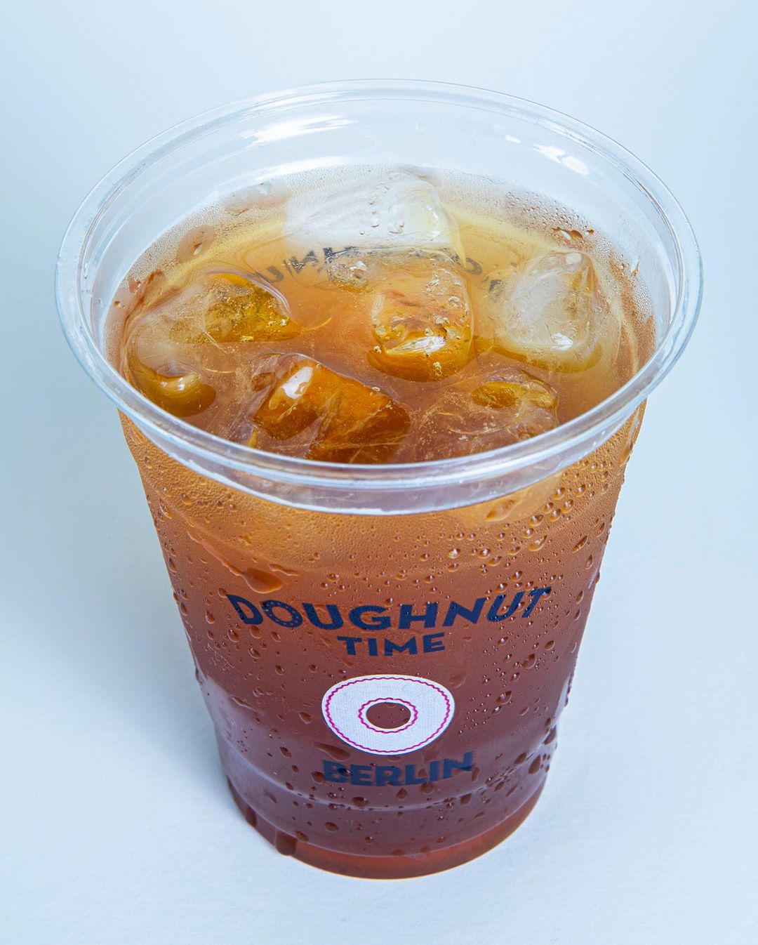 Iced tea served in a branded plastic cup with logo, displaying the 'Doughnut Time Berlin' logo on a transparent plastic cup filled with ice, highlighting clear and vibrant branding.