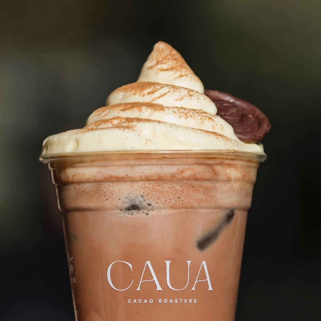 Rich chocolate iced drink topped with whipped cream and cocoa powder in a Personalised Milkshake Cup with Caua Cacao Roasters branding, perfect for a decadent treat.