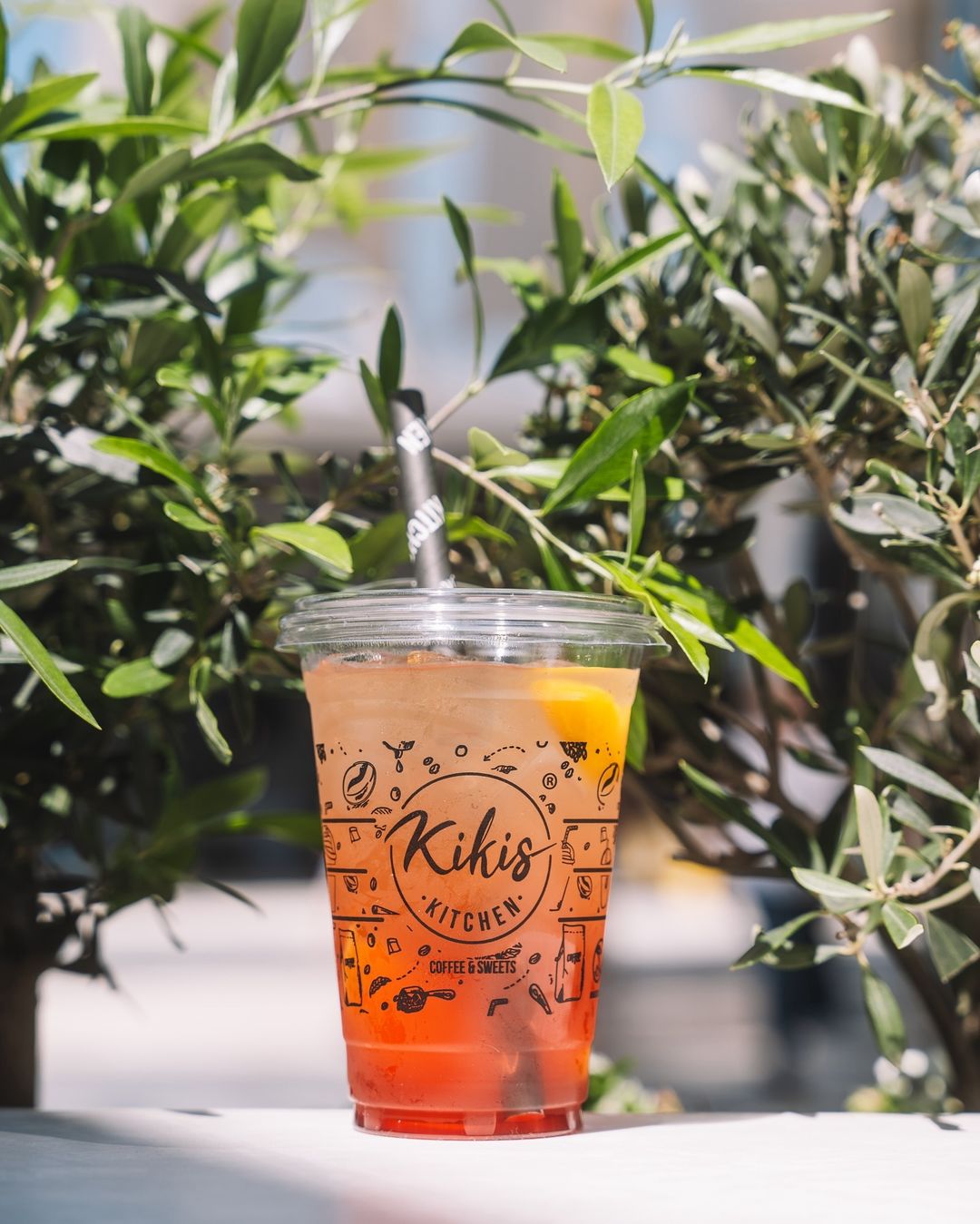 Refreshing iced drink served in a branded plastic cup with logo from 'Kiki's Kitchen,' featuring colorful layers and a black straw.