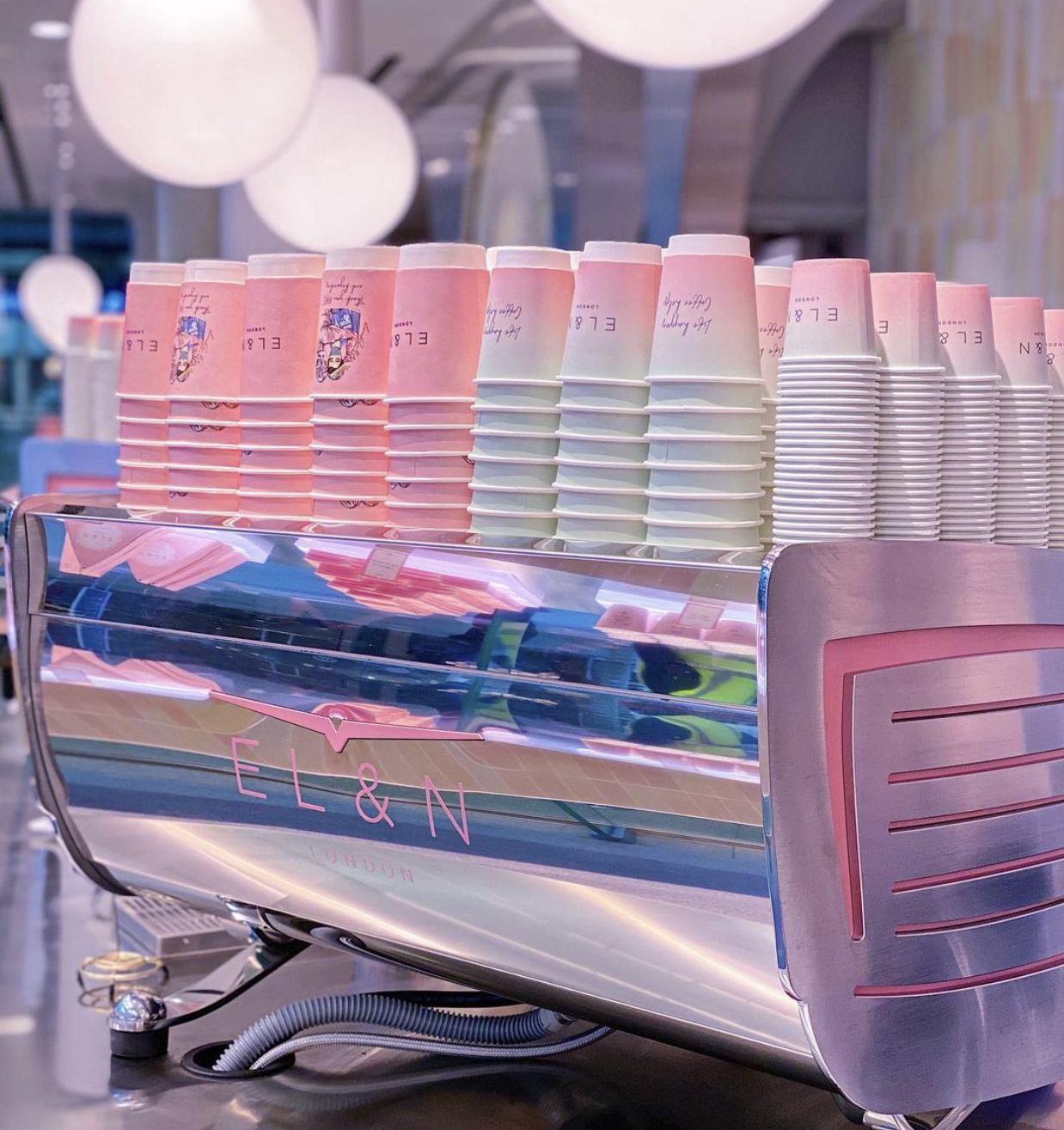 Stacks of pink and white branded paper cups displayed on a café espresso machine, adding a stylish and vibrant look to the coffee station.